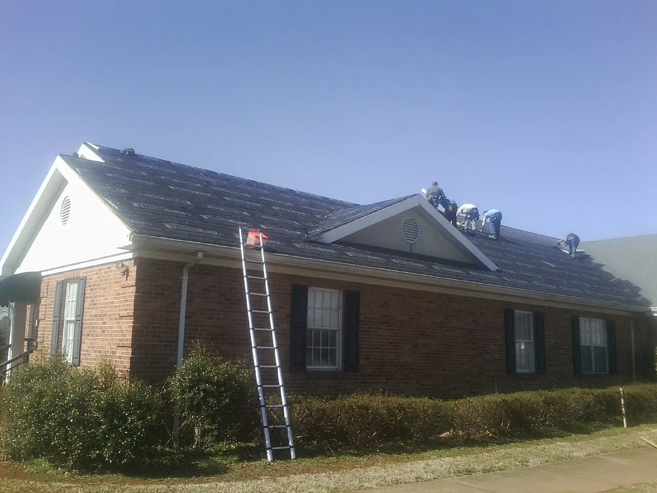 Crew tearing shingles off a brick ranch roof with a ladder set — Metal Roof Repair work by our crew in Estacada