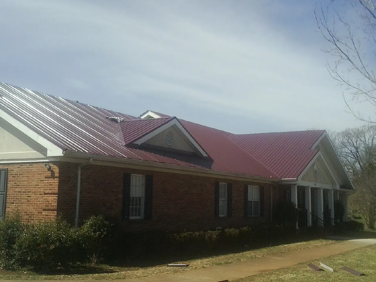 Red metal roof with gabled entries on a long brick building, from a Hail Damage Roof Repair job in Estacada