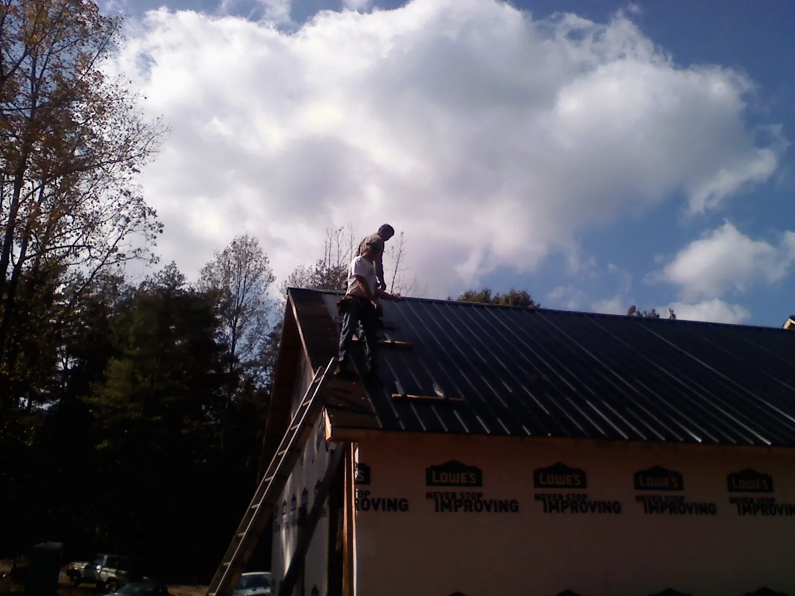 Roofer fastening dark metal panels high against a cloudy sky, from a Roof Inspection job in Estacada