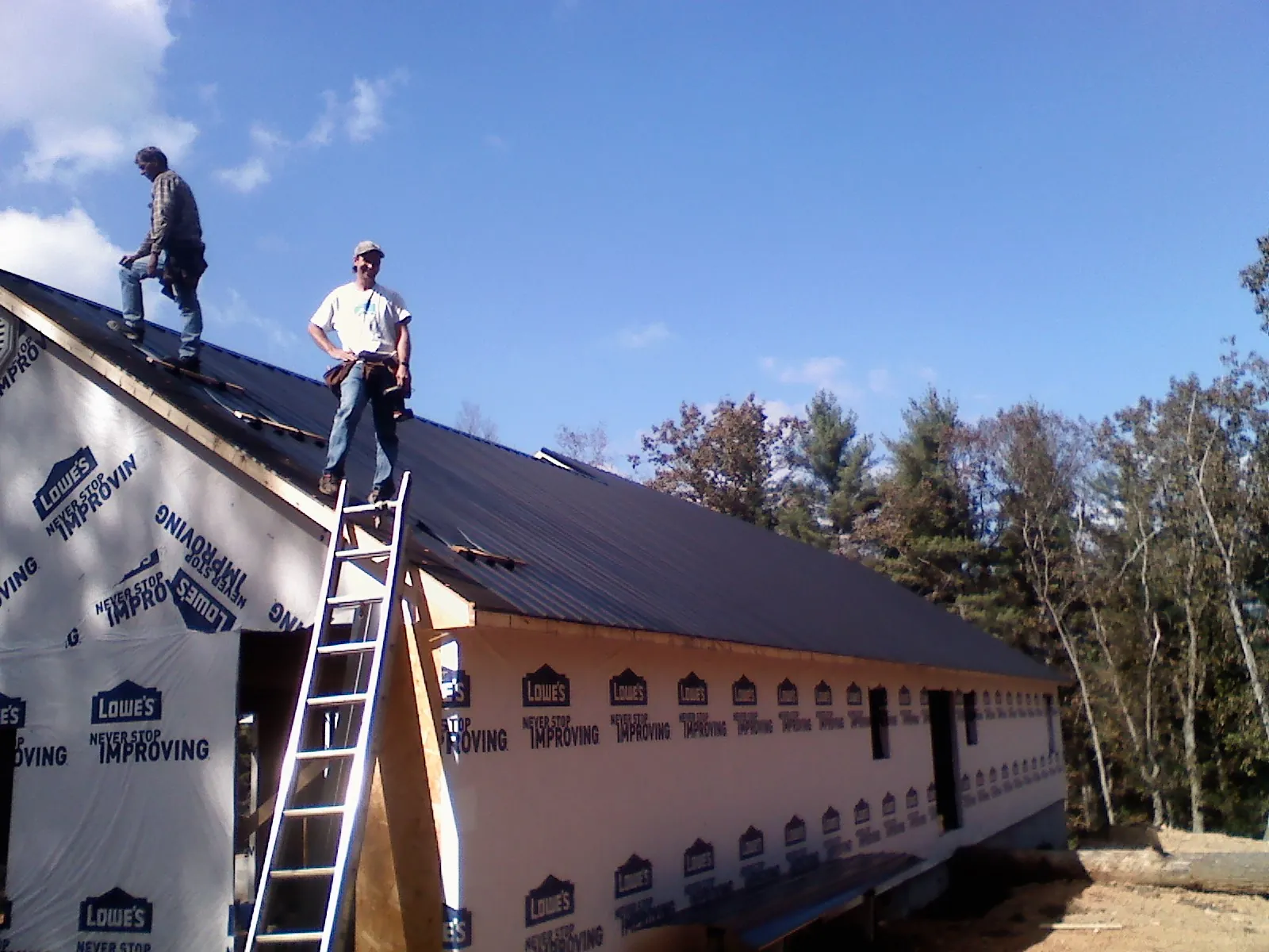 Two roofers standing on a long dark metal roof over a wrapped building in Estacada