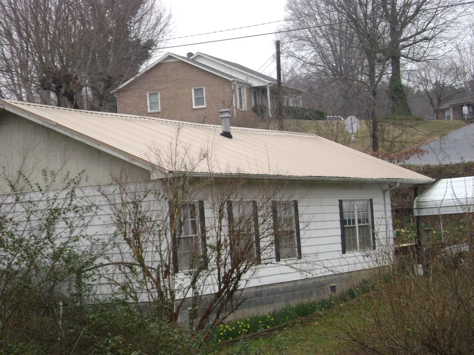 Tan metal roof on a white sided house set into a hillside — Commercial Roofing by Roofing Brothers in Estacada